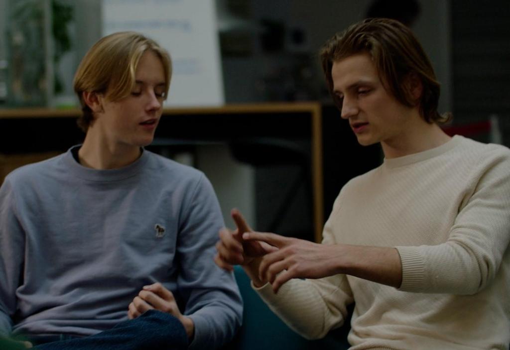 To unge gutter sitter og snakker. Den ene viser noe med hendene. Foto. 