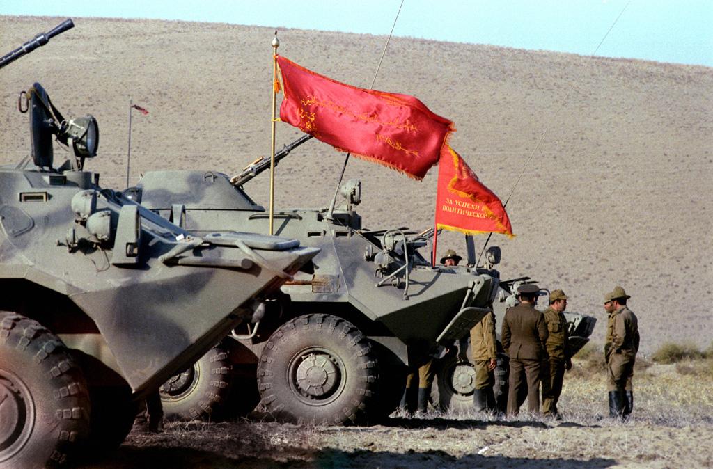 Russiske soldater står foran stridsvogner med røde flagg i et goldt landskap. Foto.