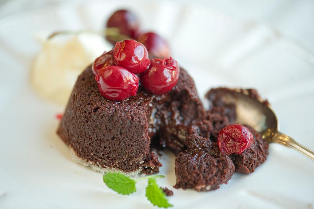Ein kvit tallerken med sjokoladefondant toppa med raude bær. Foto.