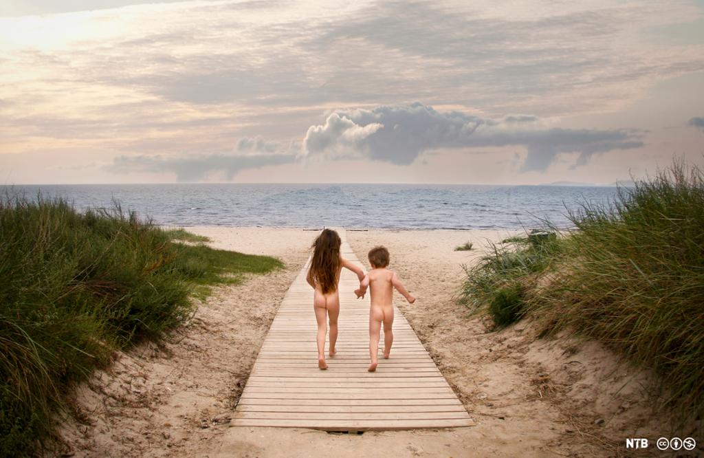 To barn springer nakne på stranda ned mot vannet. Foto.