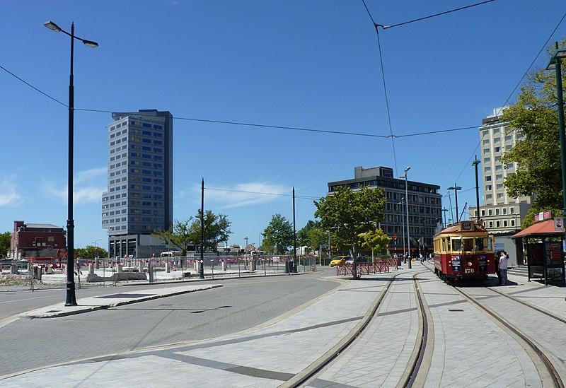 Photo: We see an urban street with a red and yellow tram. 