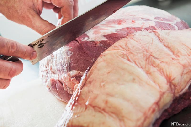 Et stort stykke kjøtt blir skåret med en kokkekniv. Foto.