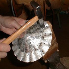 Sølvplate blir forma ved hjelp av hammararbeid. Foto.