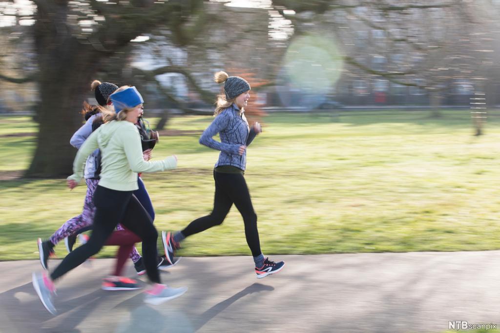 Ei gruppe kvinner løper på ein asfaltert gangveg i ein park. Foto.