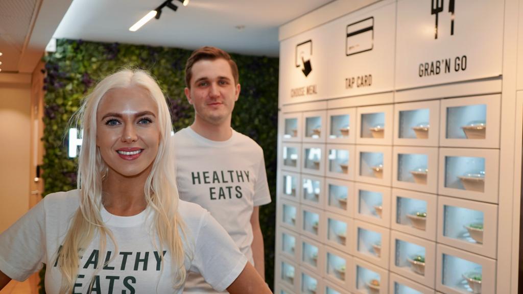 Healthy EATS-gründerane Vilde Regine Tellnes og Arve Førland står framfor ein Healthy EATS Food Wall (matvegg). Dei har på seg kvar si t-skjorte med Healthy EATS-logo. Foto.