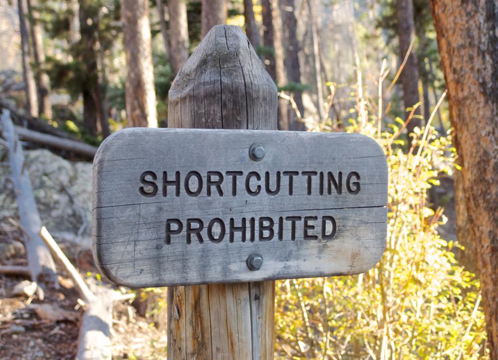 A wodden sign showing the words shortcutting prohibited. Photo. 