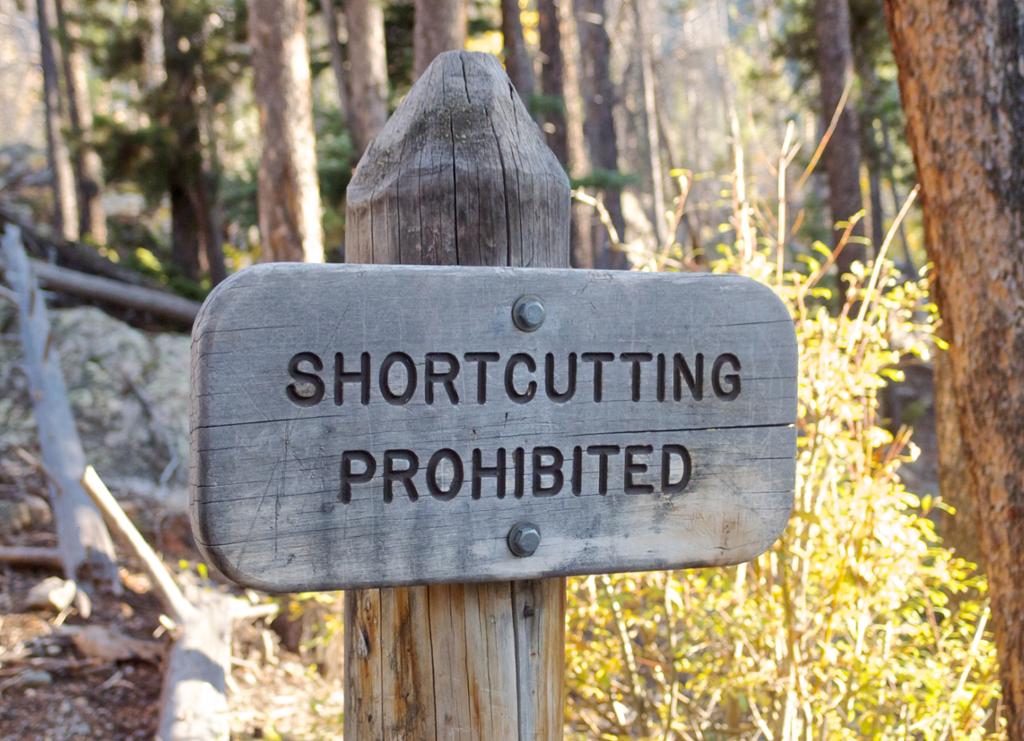 A wodden sign showing the words shortcutting prohibited. Photo.