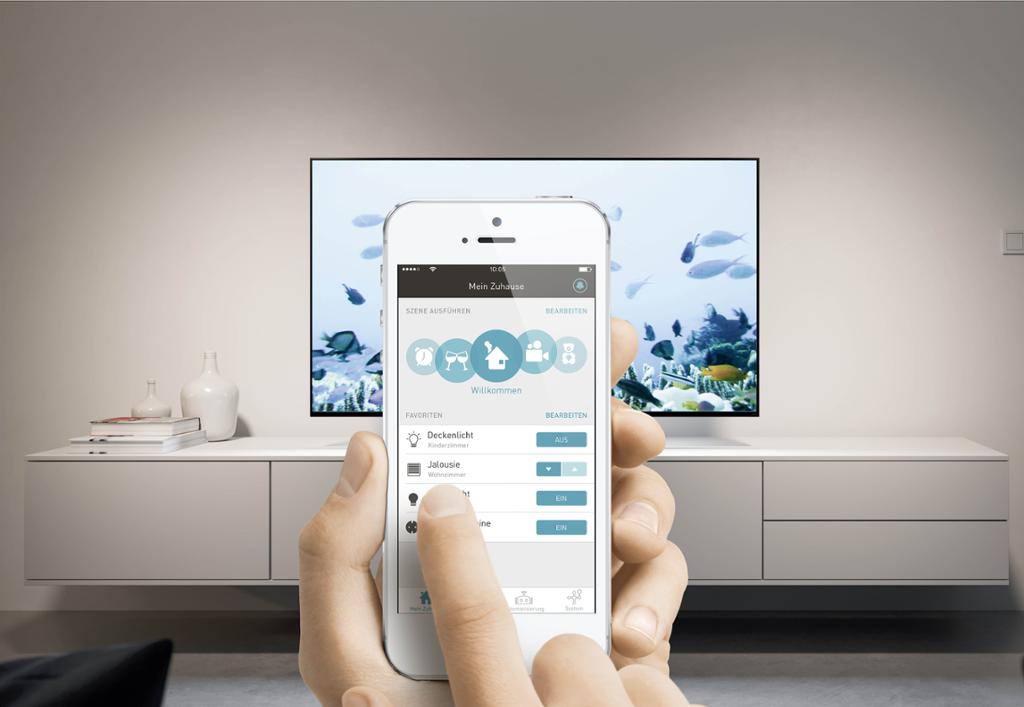 Nærbilde av en mobiltelefon. På skjermen ser vi en app som styrer ulike smarthusfunksjoner, og i bakgrunnen ser vi en TV på en moderne TV-benk. Foto.