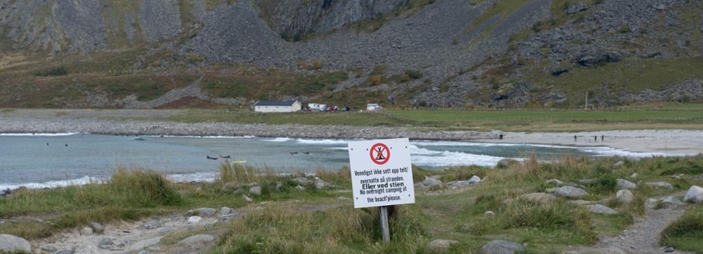 Et forbudsskilt på en strand i Lofoten. Her er det forbudt å sette opp telt og overnatte på stranden eller ved stien. Dette for å sikre bærekraft og verne om naturen. Fotografi. 
