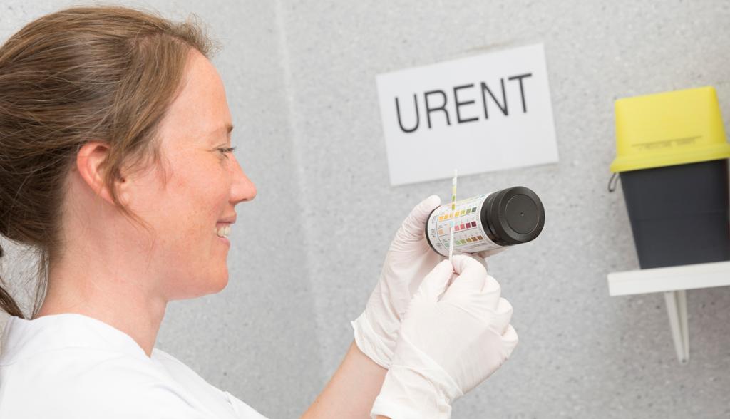 Sykepleier sjekker fargekoder på en urinprøve i uren sone. Foto.