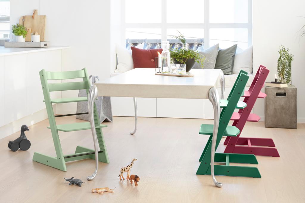 Et hvitt spisebord i hvite kjøkkenomgivelser med tre fargede Tripp Trapp-stoler rundt. Foto. 
