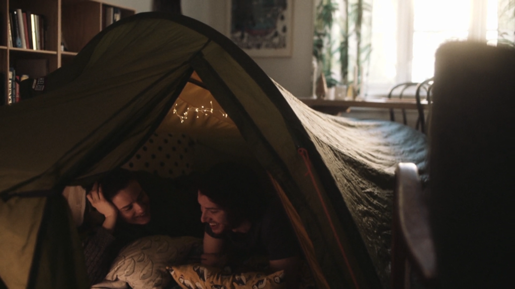 Ungt par ligger i telt i stua. Foto.
