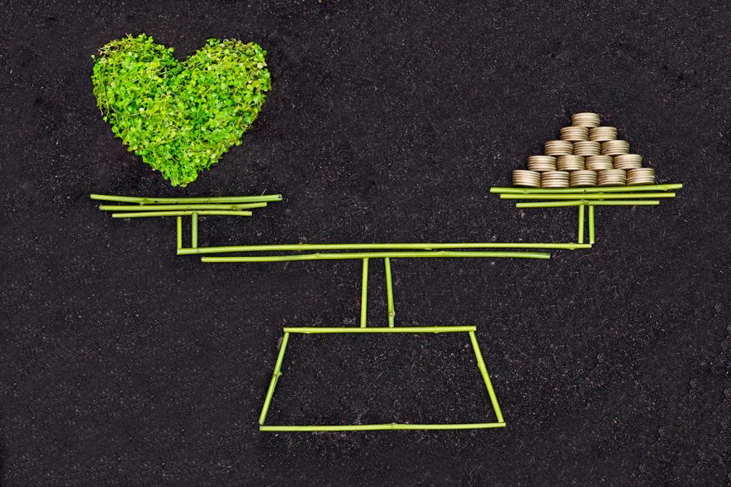 En vekt i likevekt med et grønt hjerte på den ene vektskålen og penger på den andre. Illustrasjon.
