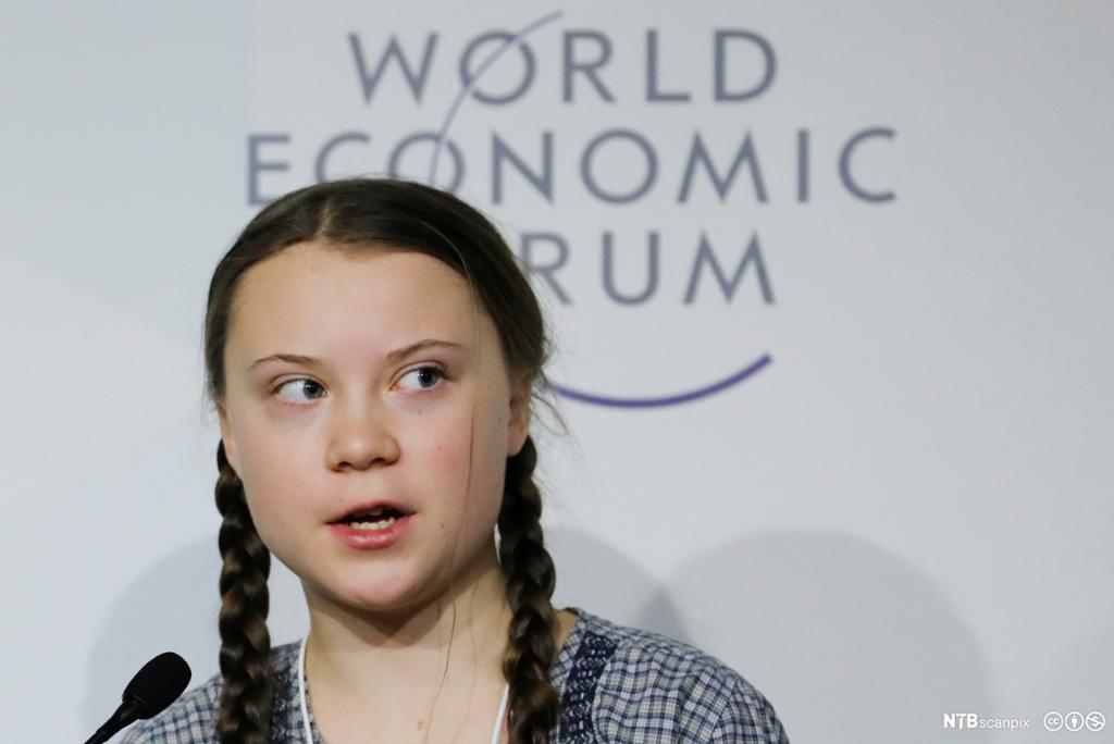 Tenåringen Greta Thunberg snakkar i mikrofon framfor logoen til World Economic Forum. Foto.