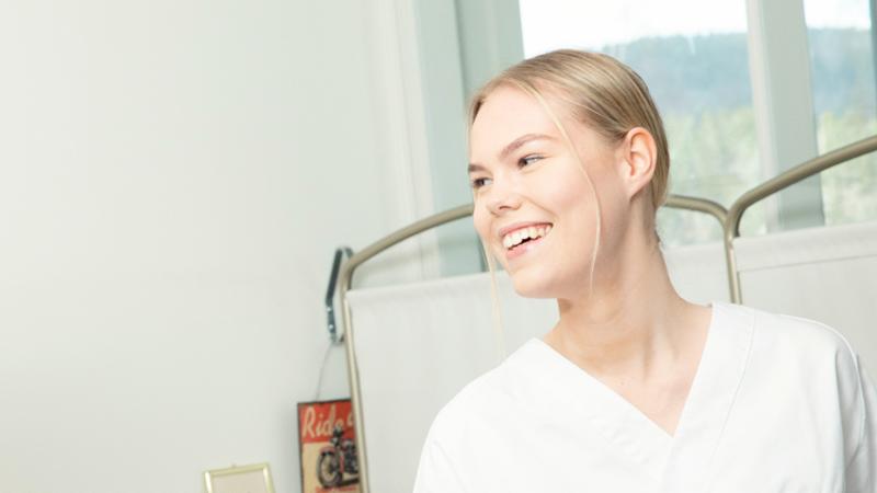 Kvinnelig helsefagarbeider smiler og kikker mot høyre. Foto.
