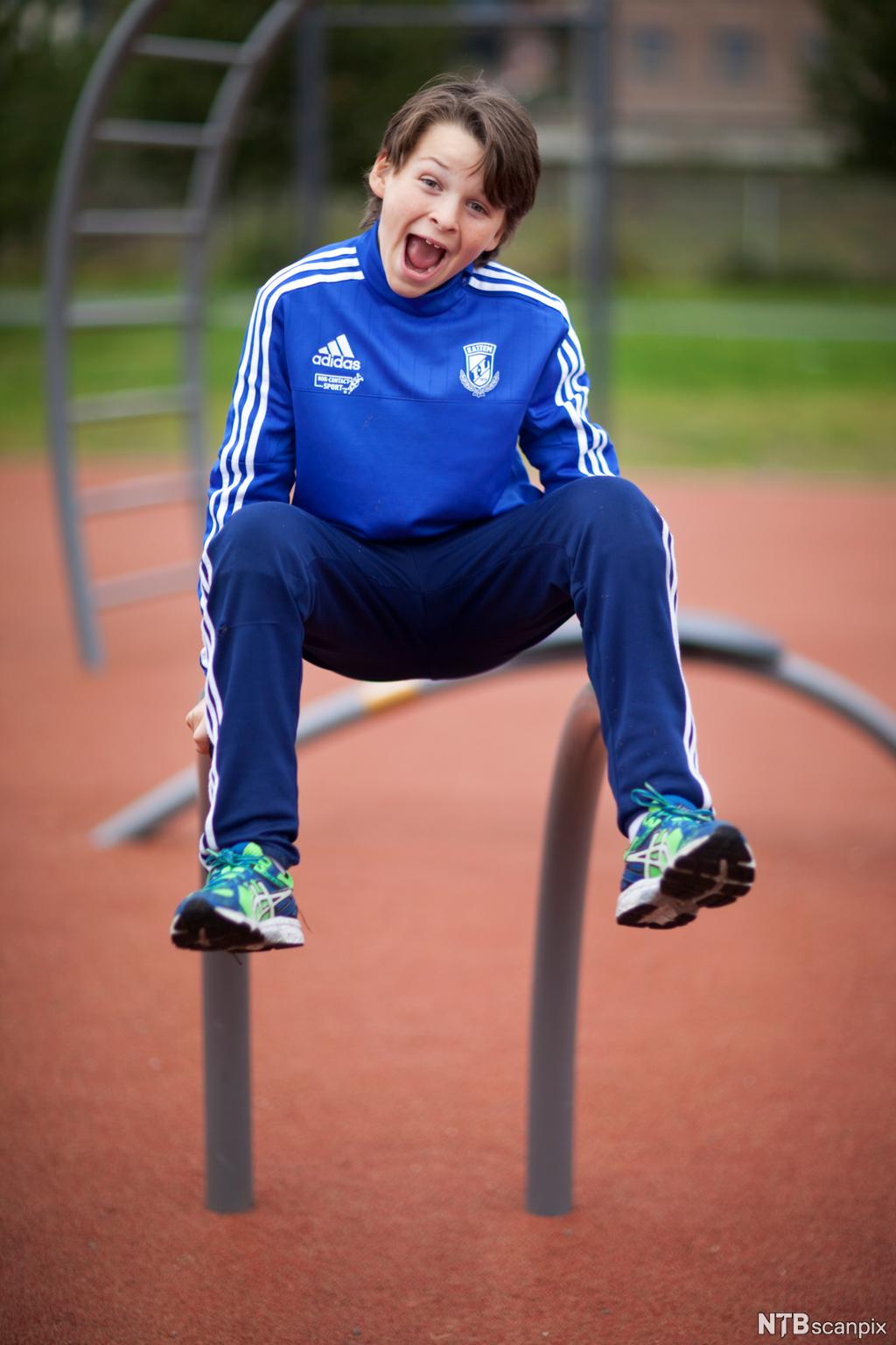 En glad gutt med treningstøy på utfolder seg i en utendørs treningspark. Foto.