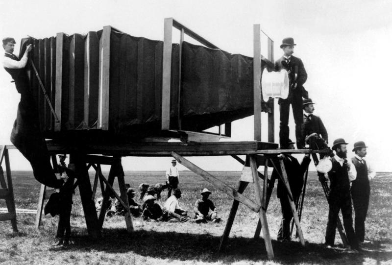 Svart-hvitt-bilde av fotograf George R. Lawrence og assistentene hans, som står på en gresslette rundt et digert kamera. Foto.