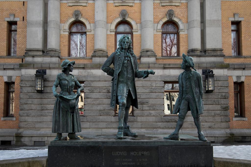 Ein bronsestatue av diktaren Ludvig Holberg framfor Nationaltheatret i Oslo. Saman med Holberg står to mindre bronsestatuar, alle kledde i 1700-talsklede. Foto.