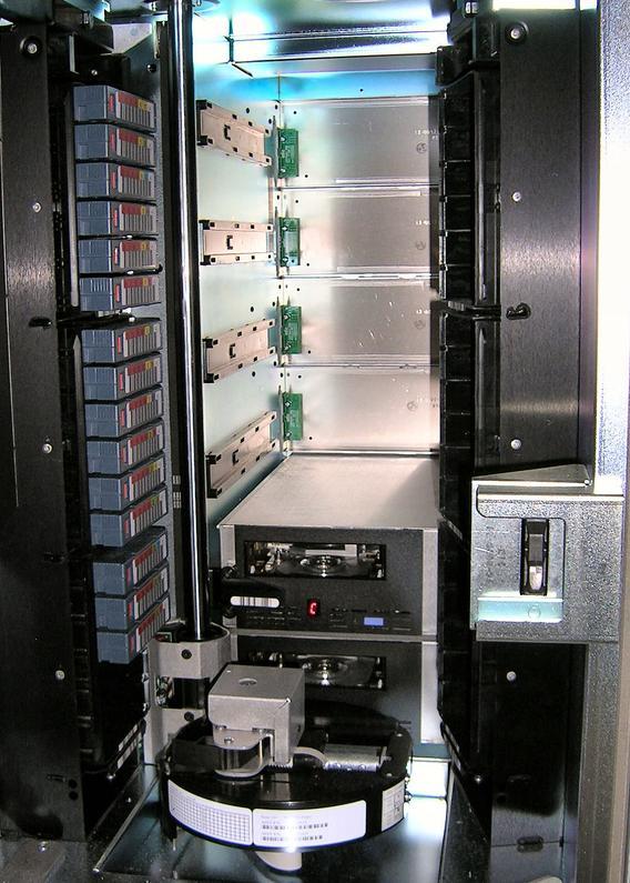 Innside av tape-robot. Datakassetter er stablet i høyden på siden. De kan plukkes ned av en robotarm til en av to tape-stasjoner som er innebygd i enheten. Foto.