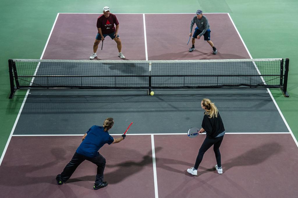 Foto av fire utøvere som spiller pickleball på en bane. 