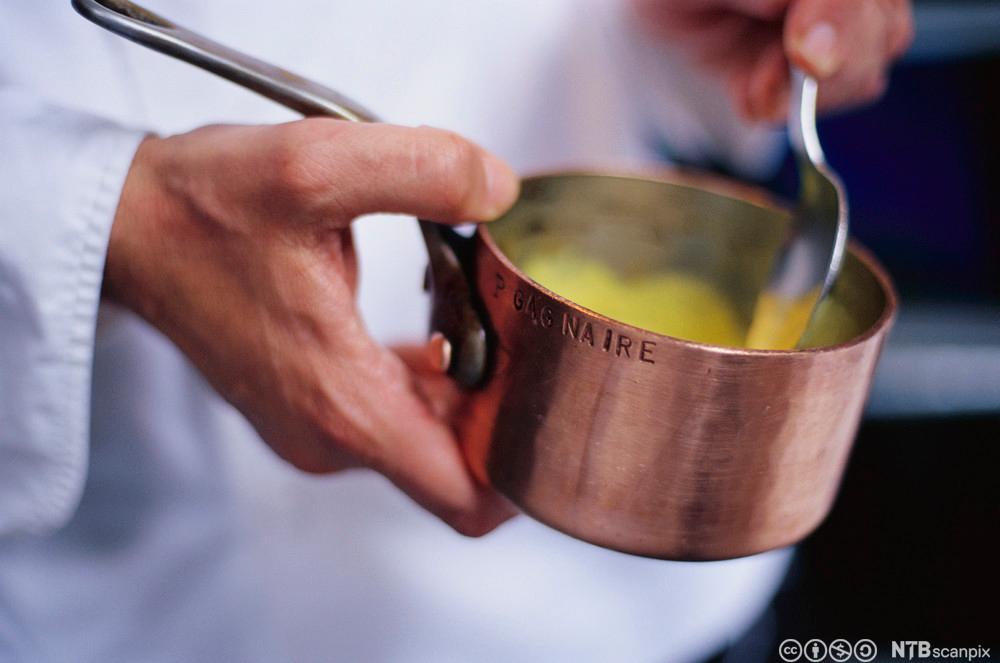 En kokk holder en liten kjele med saus i hendene. Foto.