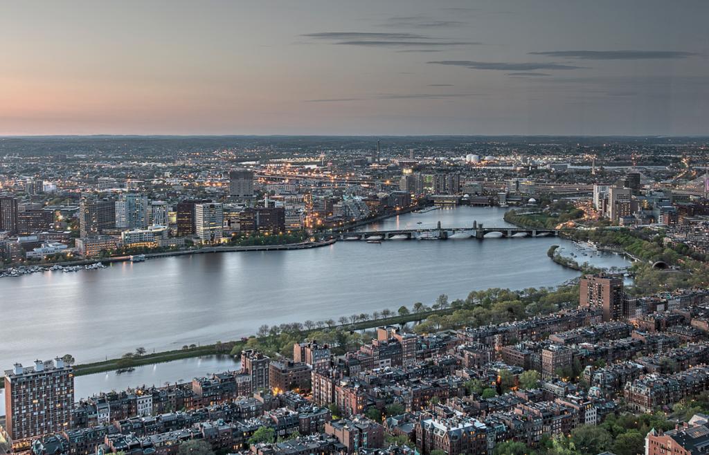 Photo: View of the city of Boston, Massachusetts, USA. We see a river with houses on both sides. The sky is slightly pink. 