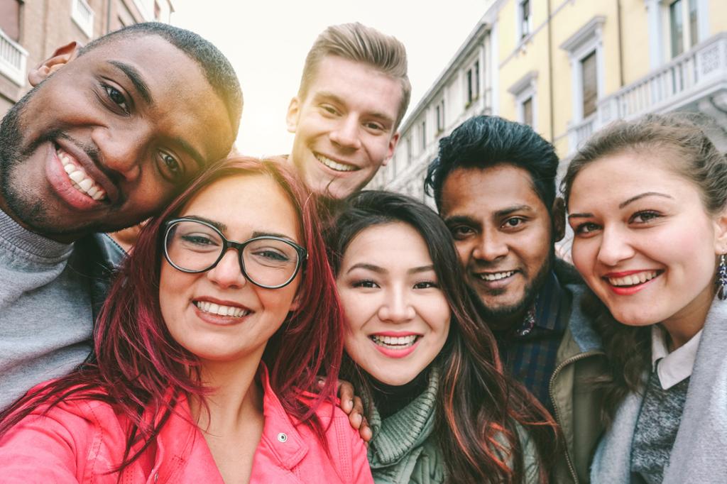Seks glade unge personar med ulik kulturell bakgrunn tek ein selfie saman. Bygardar i bakgrunnen. Foto.