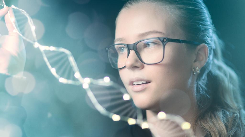 Jente med briller holder en DNA tråd mellom fingrene. Foto.