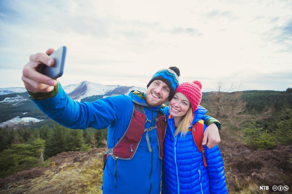 En mann og en kvinne tar en selfie i fjelllandskap. Foto