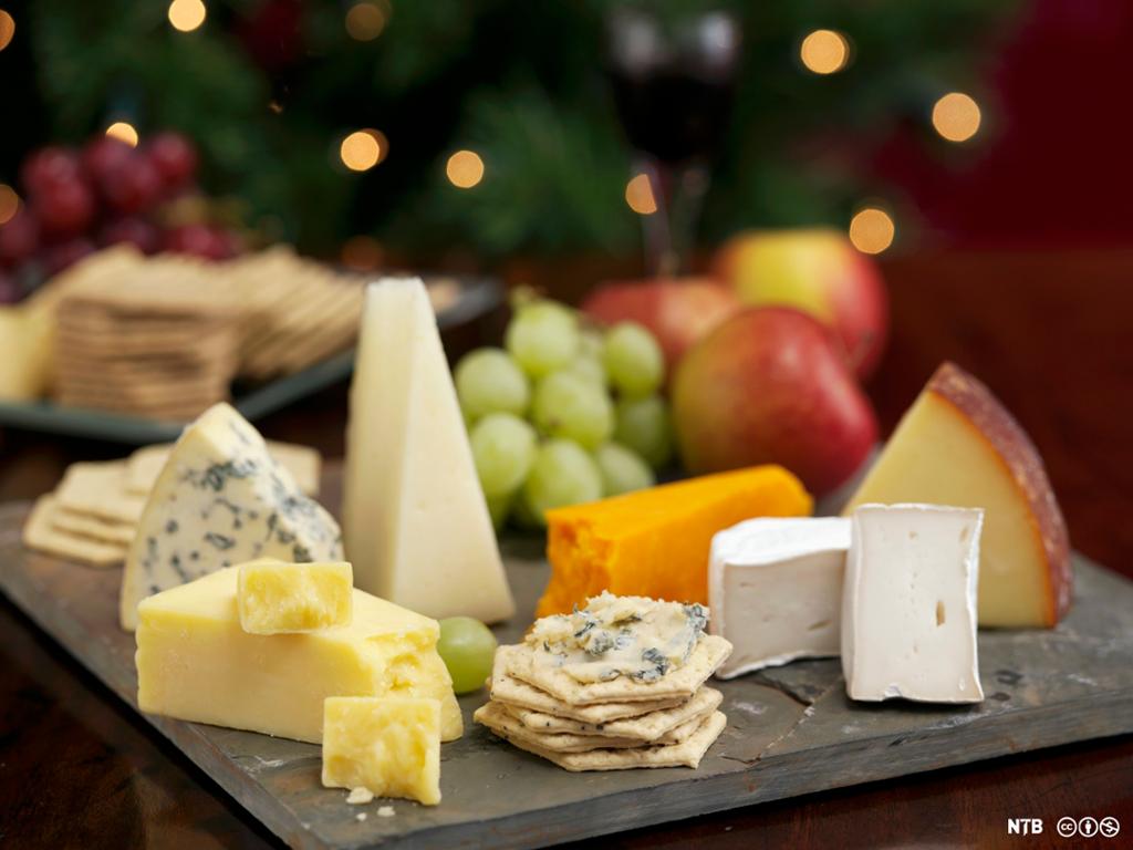 En osteanretning med ulike typer ost, kjeks og frukt. Foto.