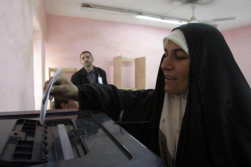 An Iraqi woman prepares to cast her ballot. A man is watching in the background.  