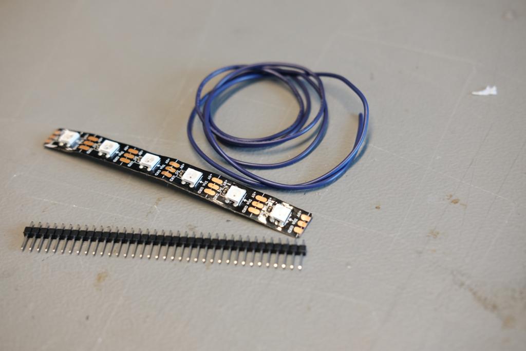 LED-stripe, leidningar og ei skjene med koplingspinnar liggande på eit bord. Foto.