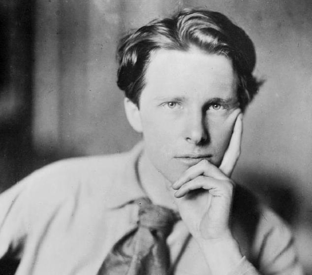 Black and white portrait of Rupert Brooke. He is a young man looking directly at the camera. He is wearing a white shirt, and a scarf tied as a tie. 
