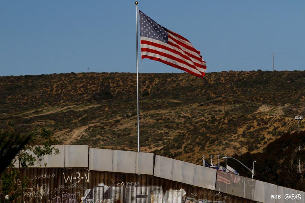 An American flag on a flag pole by the Mexican-American wall. Photo. 