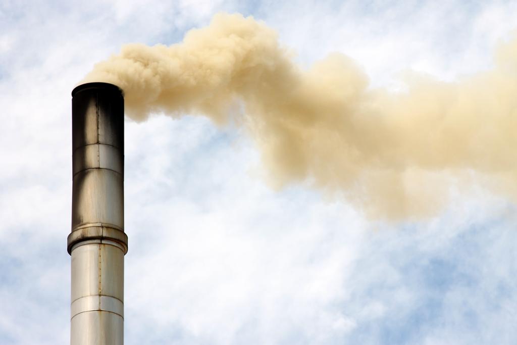 Factory chimney, beige smoke, blue sky with white clouds. Photo.