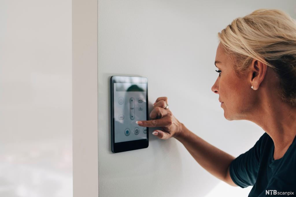 Kvinne som betjener et digitalt panel på en vegg for å styre temperaturen. Foto.