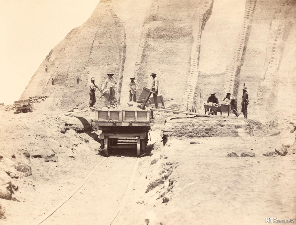 Arbeidsfolk står på tralle i et gruveområde. Foto.