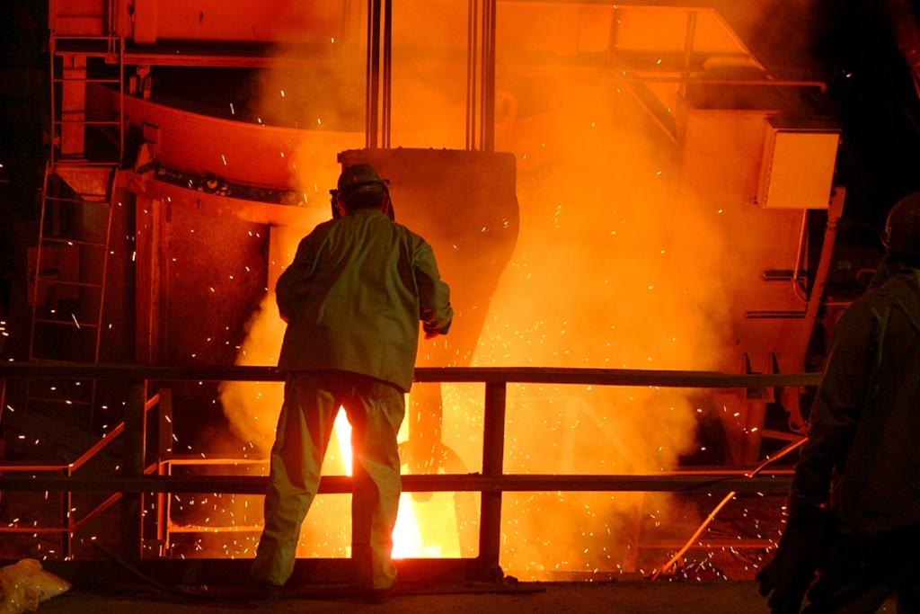 Person som står framfor ein stor smelteomn full av glødande og flytande metall. Foto.