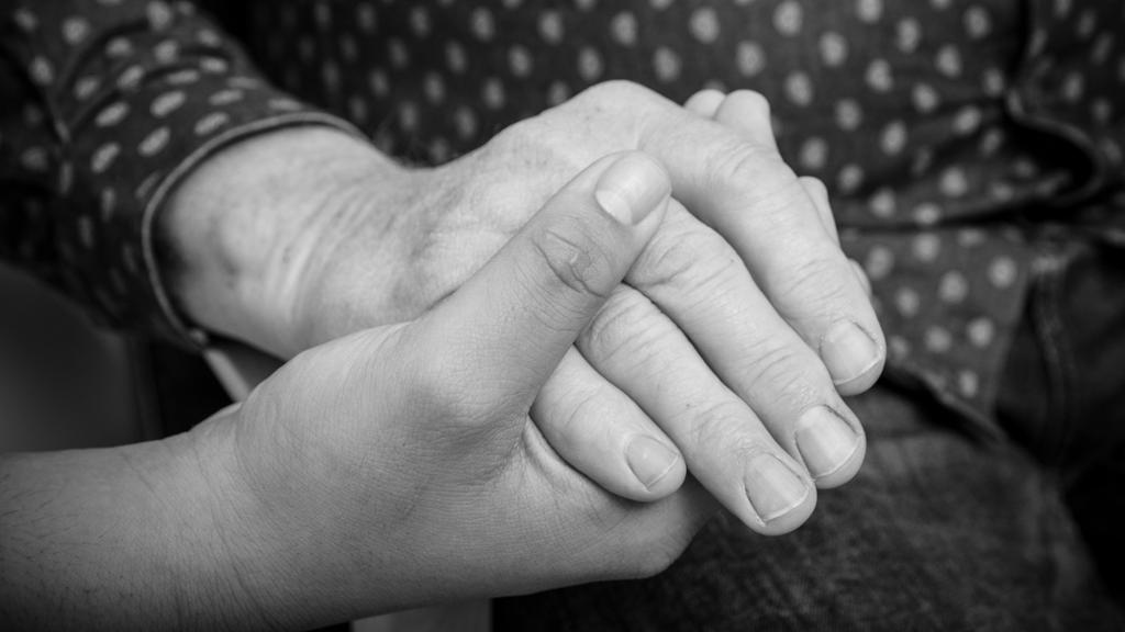Hånda til en ung person holder rundt hånda til en eldre person. Foto.