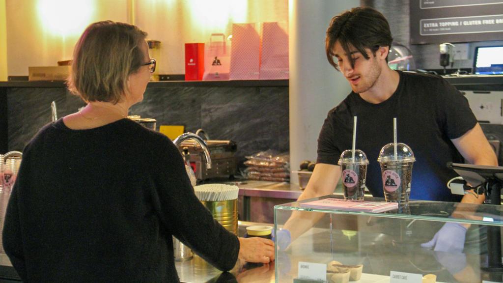 Dame får servert kaffe over disk av mann. Bildet er tatt i Joe and the Juice sine lokaler på Lagunen kjøpesenter ved Bergen i oktober 2020