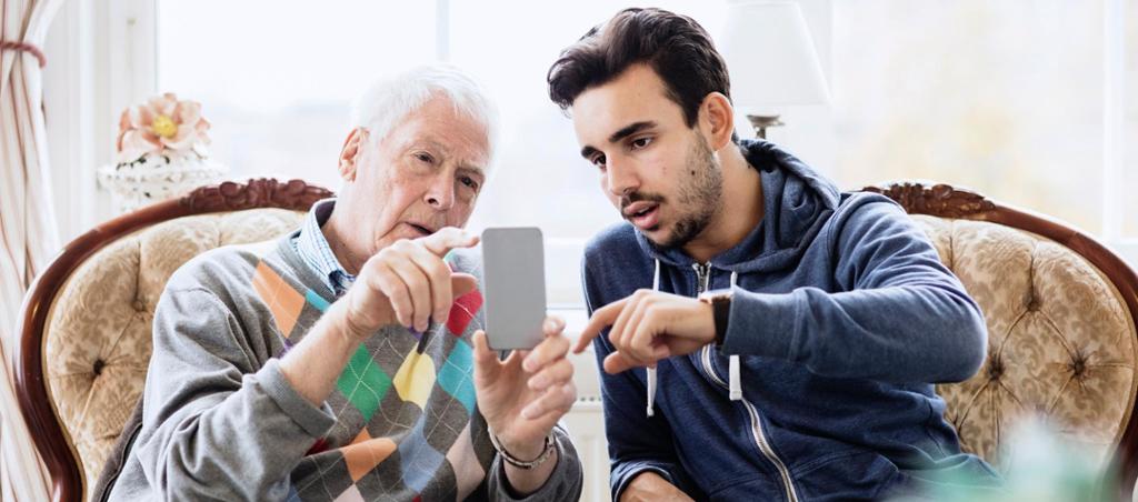 Ein eldre og ein yngre person samtalar og peiker på ein mobilskjerm. Foto.