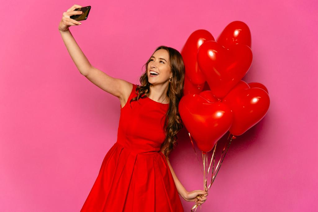 Kvinne tar selfie, holder ballonger og smiler til kameraet. Foto.