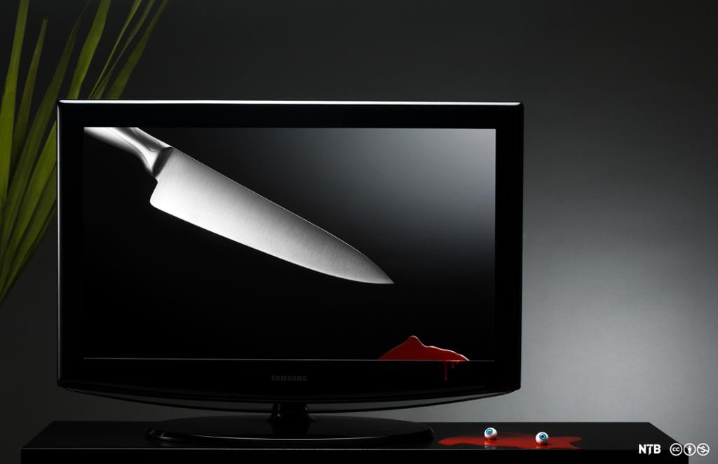 En svart TV står på en svart benk. På TV-en er det bilde av en kniv, og på benken og nederst på skjermen er det blodsøl. I blodet ligger to øyeepler. Foto.