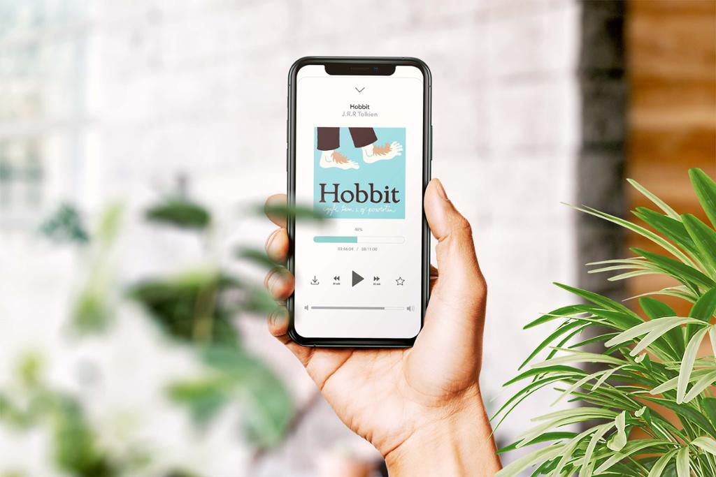En hånd holder en mobil med lydbok-app. Appen viser lydboka Hobbit og en avspiller. Foto.

