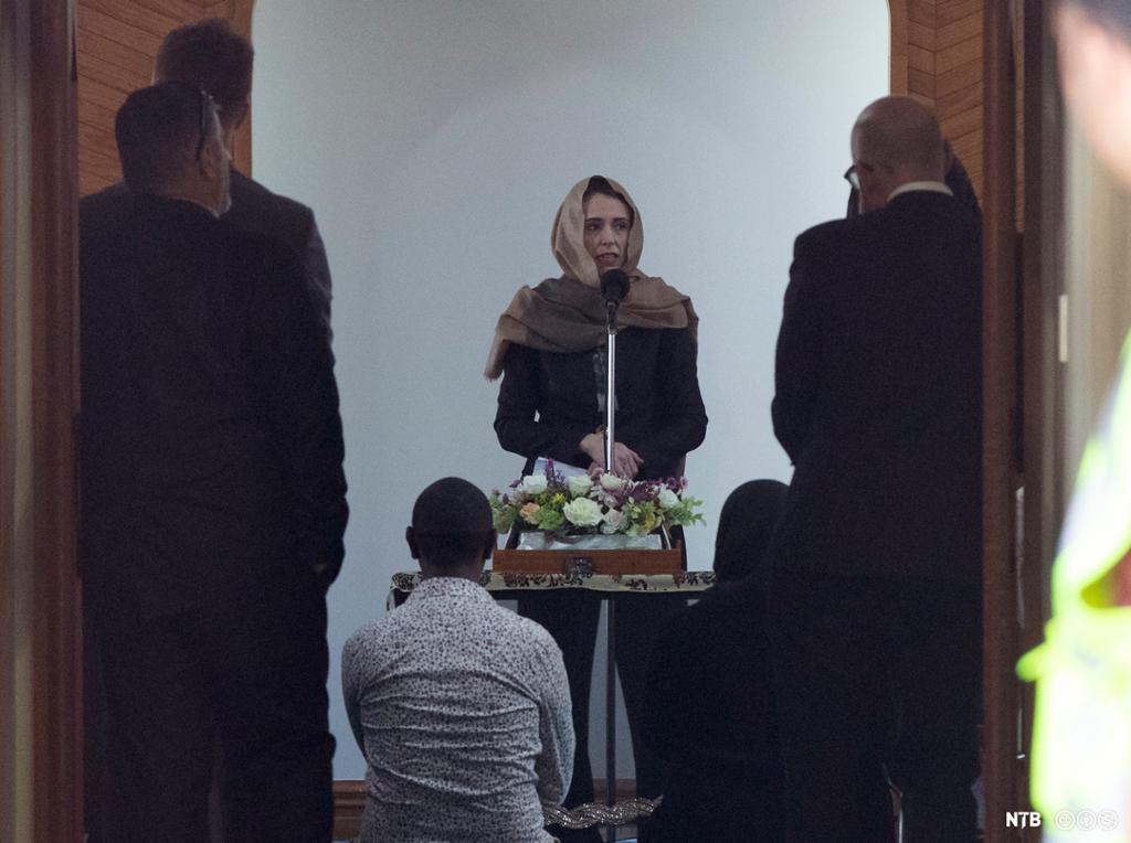 Prime Minister Jacinda Ardern, facing front, talks to members of the Muslim community inside the Al Noor Mosque in Christchurch. She's wearing a traditional headscarf. We only see the backs of her audience.  