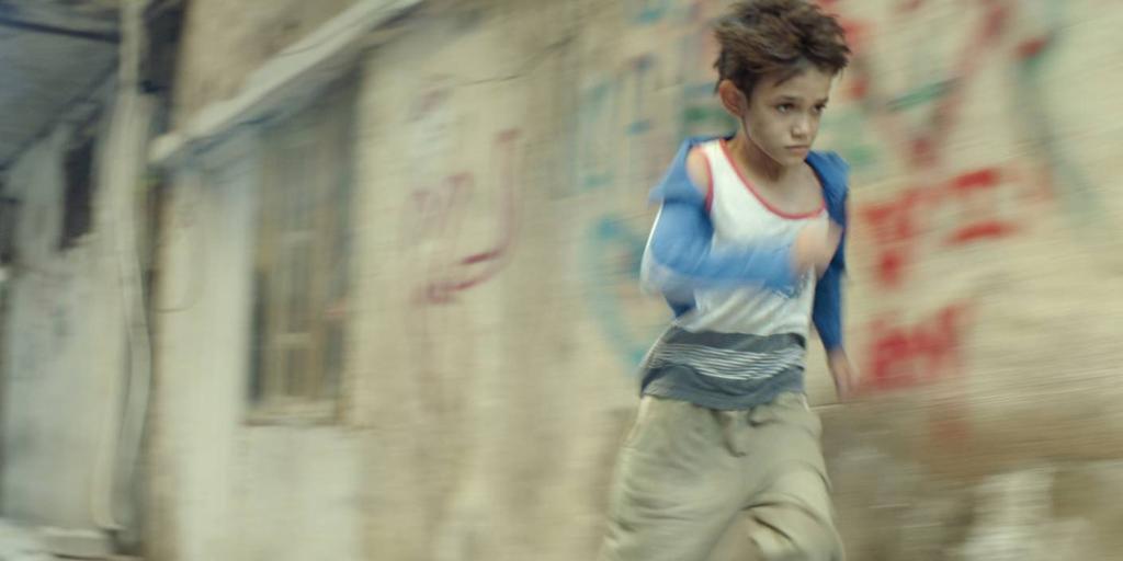 Gutt med fattigslige klær som løper. Scenebilde fra filmen Kapernaum. Foto.