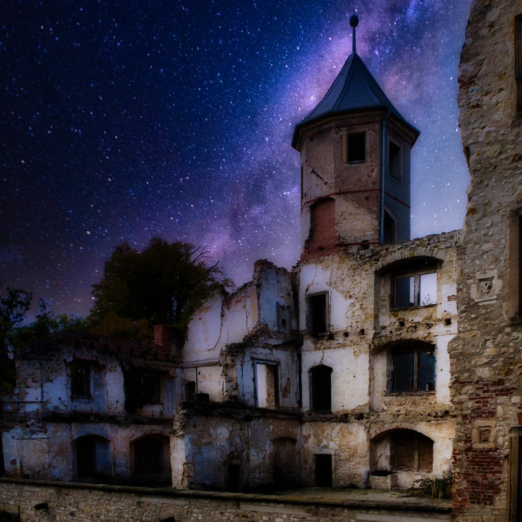 Ruins of a castle at night. There are lots of stars in the sky. Photo. 