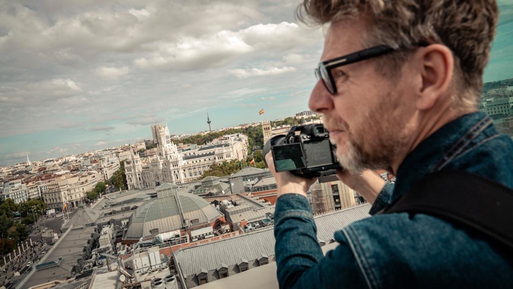 En mann står på en takterrasse og ser over Madrid mens han holder et kamera. Foto.