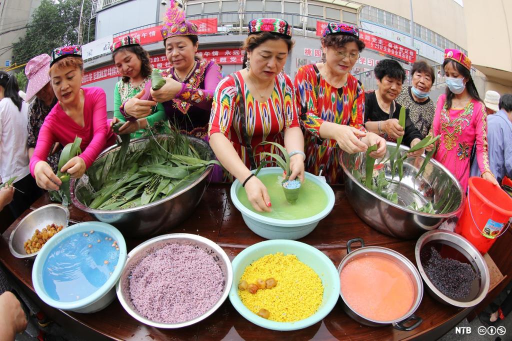 Photo: Seven women of Asian origin are preparing food. In front of them are bowls filled with food in many different colours. 