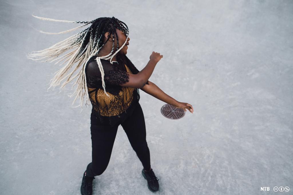 Tenåringsjente med mørkt hår som er lyst i endene, slenger på håret så de lange flettene danser. Foto.
